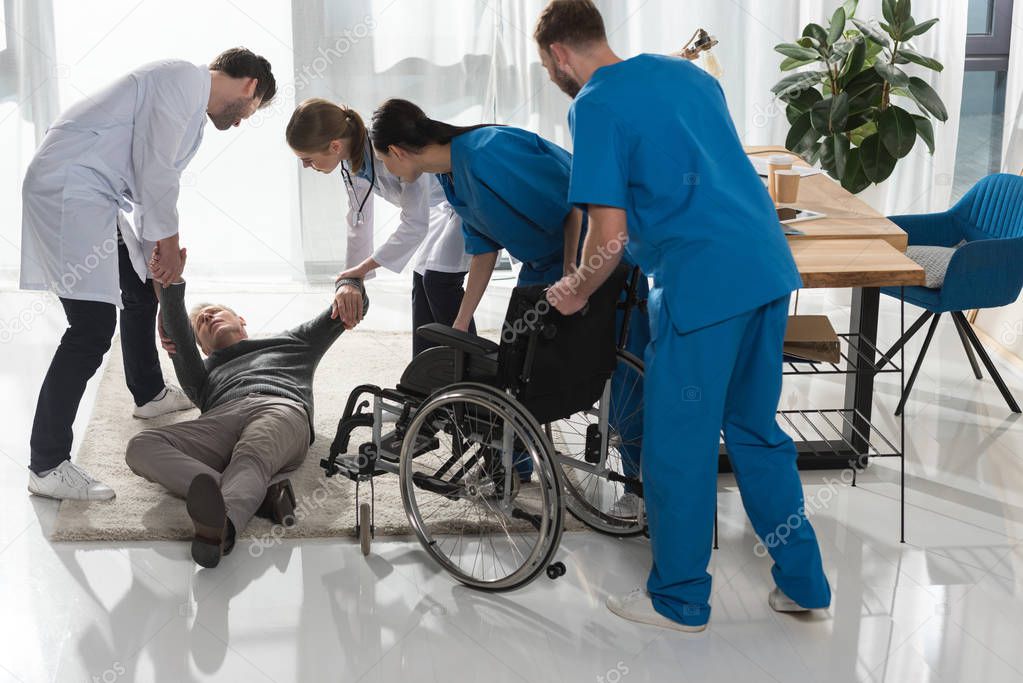 doctors helping fell mature man to sit on wheelchair