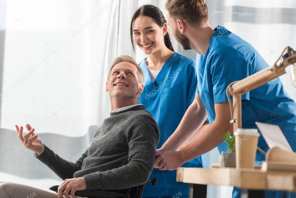 smiling doctors and patient on wheelchair talking in the hospital