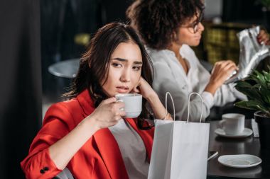depressed young woman drinking coffee after shopping clipart