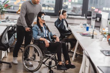 woman in wheelchair using virtual reality glasses at modern office clipart