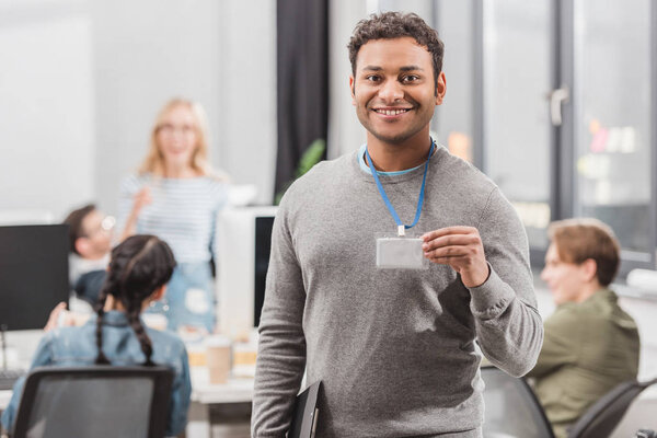 happy african american man showing name tag at modern office