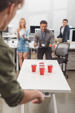 young attractive people playing beer pong at modern office after work clipart
