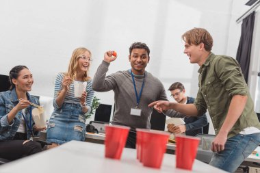young attractive workers playing beer pong at modern office after work clipart