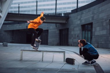 man taking photo of skateboarder doing trick over bench clipart