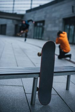 skateboarders taking photos of tricks with skateboard leaning at bench on foreground clipart