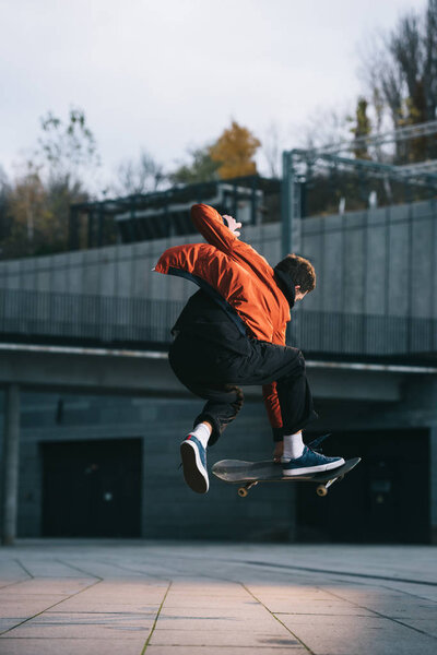 skateboarder in red jacket performing jump trick in urban location