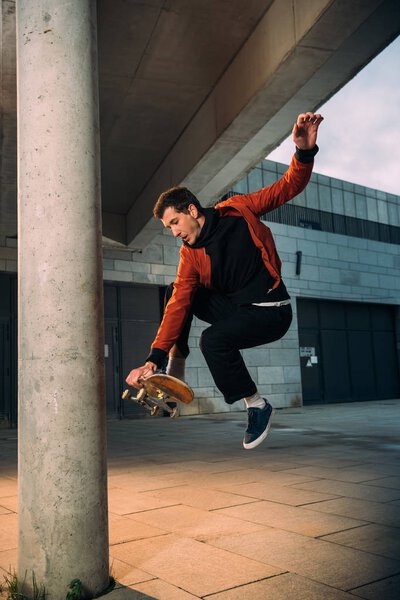 stylish young skateboarder performing jump trick in urban location