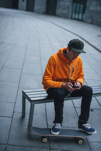 Skater Siedząc Ławce Słuchanie Muzyki Smartfona — Zdjęcie stockowe