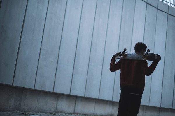 skateboarder standing with board on shoulders in front of grey concrete wall