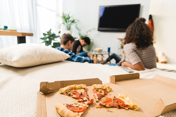 друзья смотрят телевизор с пиццей на переднем плане
 