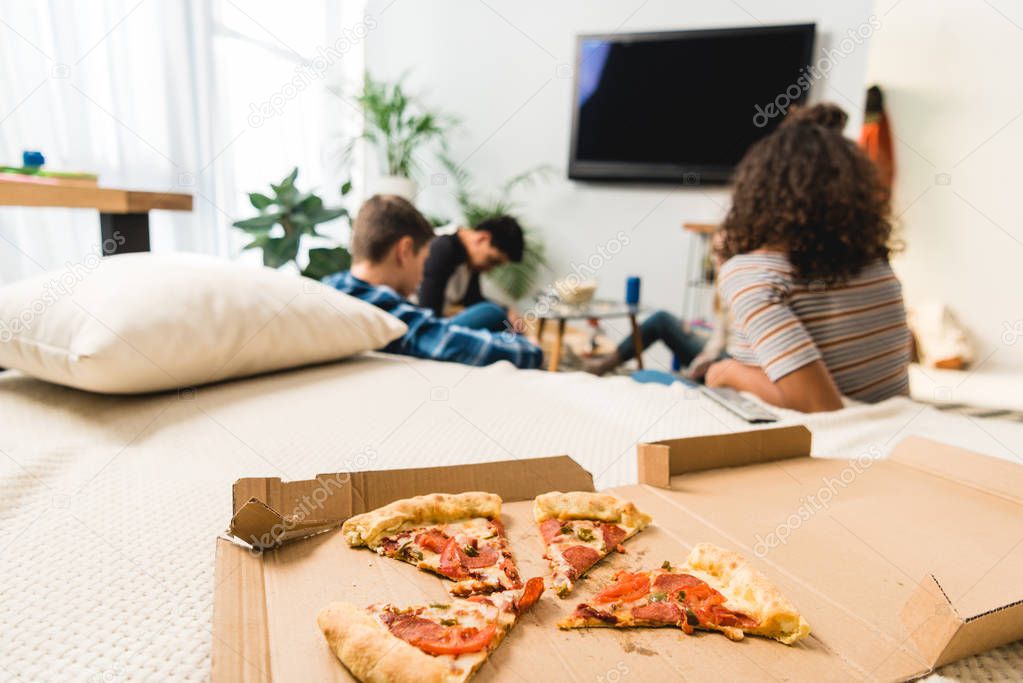 friends watching tv with pizza on foreground 