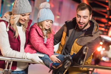 happy parents looking at cute little daughter wearing skates on rink  clipart