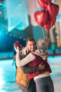 hediye kutusu ve sarılma mutlu erkek arkadaşıyla kalp tutan genç kadın pisti üzerinde balon şeklinde 