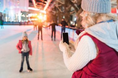 sevimli küçük kızını buz pateni pisti üzerinde çekim smartphone ile genç kadın