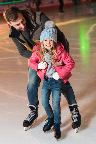 beautiful happy father and daughter hugging and having fun while skating on rink