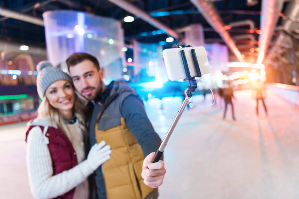 selective focus of happy young couple taking selfie with smartphone on rink
