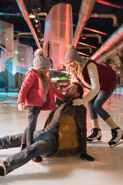 молодая женщина с милой дочерью, смотрящая на смеющегося мужчину падающего на каток
