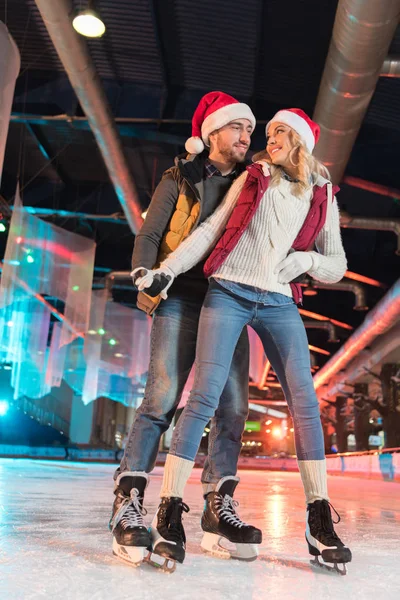 Schönes Glückliches Junges Paar Weihnachtsmannhüten Beim Schlittschuhlaufen Auf Der Eisbahn — Stockfoto