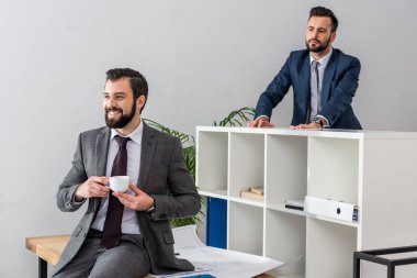 colleague looking above partition on businessman holding cup of coffee and talking with someone clipart