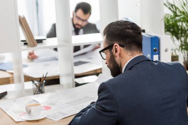 businessmen sitting at working tables with shelves between them clipart
