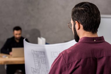 rear view of architect looking at blueprint in office clipart