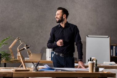 smiling architect standing near working table and looking away clipart