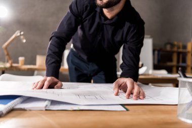 cropped image of architect looking at blueprints on table
