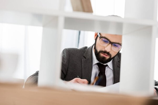 взгляд через перегородку на бизнесмена, работающего за столом
