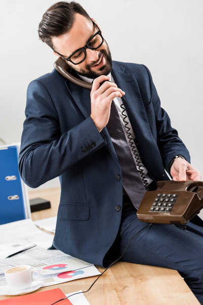 smiling businessman talking by stationary telephone in office