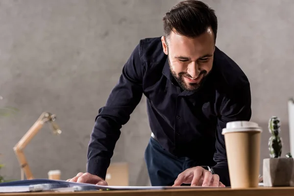 Lächelnder Architekt Beim Betrachten Von Entwürfen Auf Dem Tisch — Stockfoto