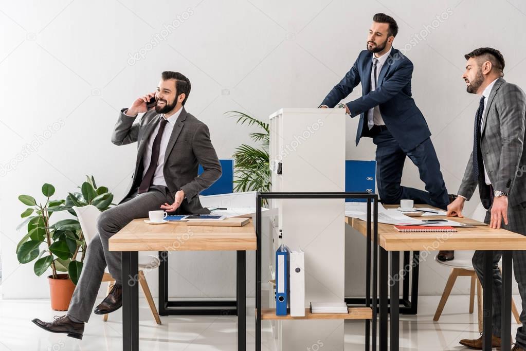 colleagues spying on businessman talking by smartphone in office