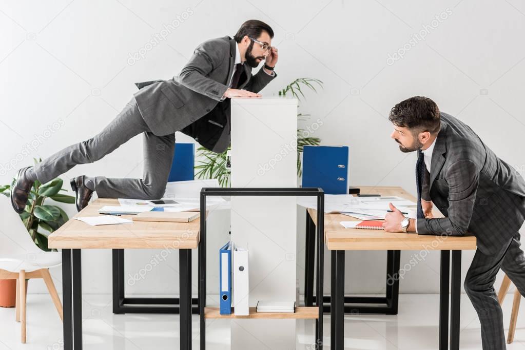 two businessmen spying on each other in office