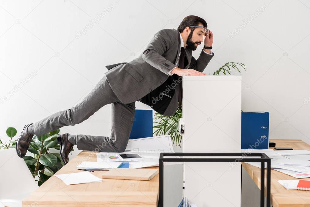 businessman spying on colleague table above partition in office