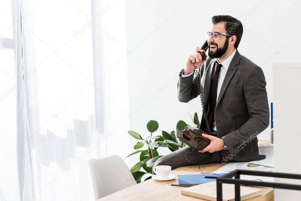 businessman talking by stationary telephone in office and sitting on table