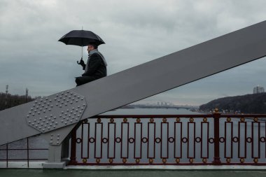 köprü inşaatı üzerinde oturan şemsiye ile yalnız adam