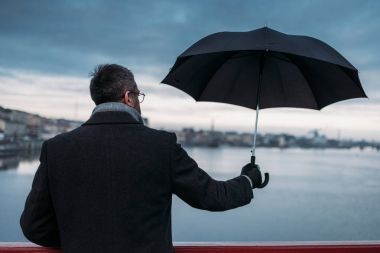 back view of lonely man with umbrella standing on bridge clipart