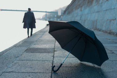 umbrella lying on river shore while man walking blurred on background clipart