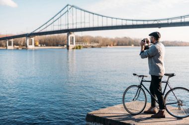 yakışıklı adam vintage film kamerası ve nehir kıyısında Bisiklet ayakta