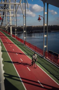 high angle view of adult man riding bicycle on pedestrian bridge over river clipart