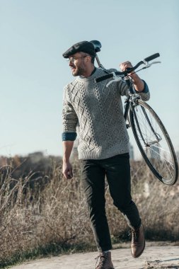 handsome adult man carrying bicycle on rural road clipart
