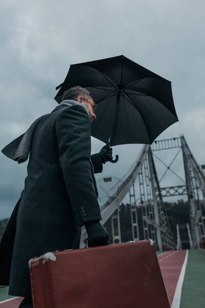 вид снизу на мужчину средних лет с зонтиком и багажом ходьба по пешеходному мосту
