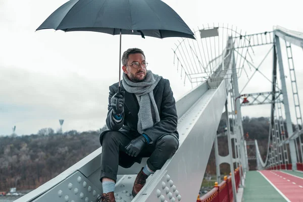 Einsamer Erwachsener Mann Mit Regenschirm Sitzt Auf Brückenkonstruktion — Stockfoto