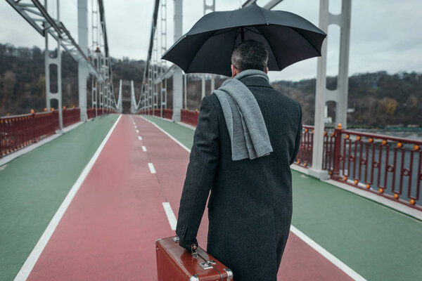 стильный человек с зонтиком и багажом ходьба по пешеходному мосту
