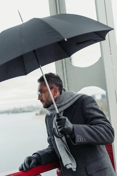 stylish adult man in scarf and coat with umbrella on bridge
