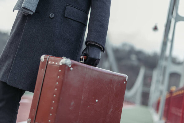 cropped shot of man in coat and gloves with suitcase