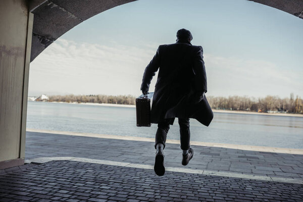 stylish man with baggage running out tunnel to river shore