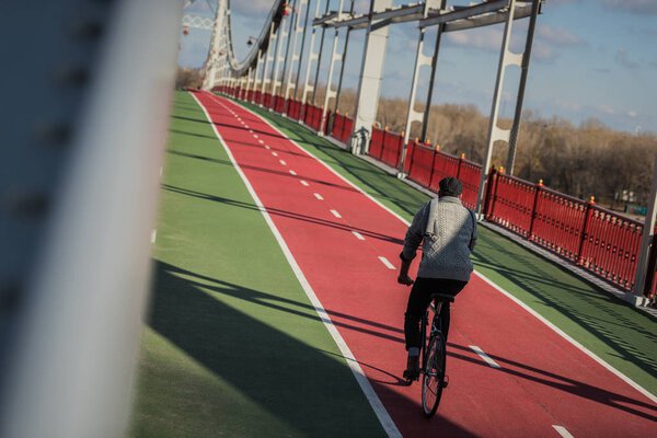 stylish man riding bicycle on pedestrian bridge with biking road