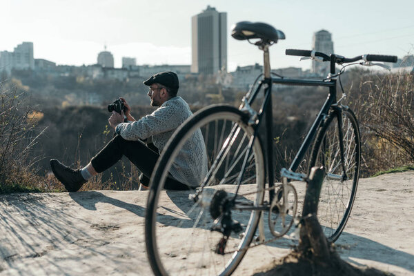 handsome adult man with vintage film camera and bicycle sitting on rural road