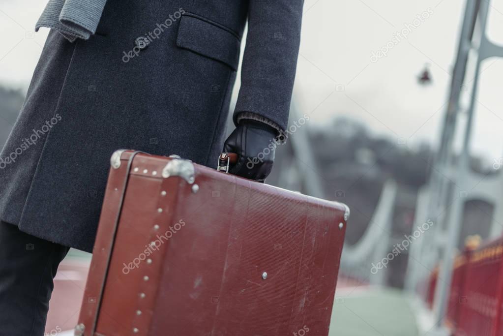 cropped shot of man in coat and gloves with suitcase