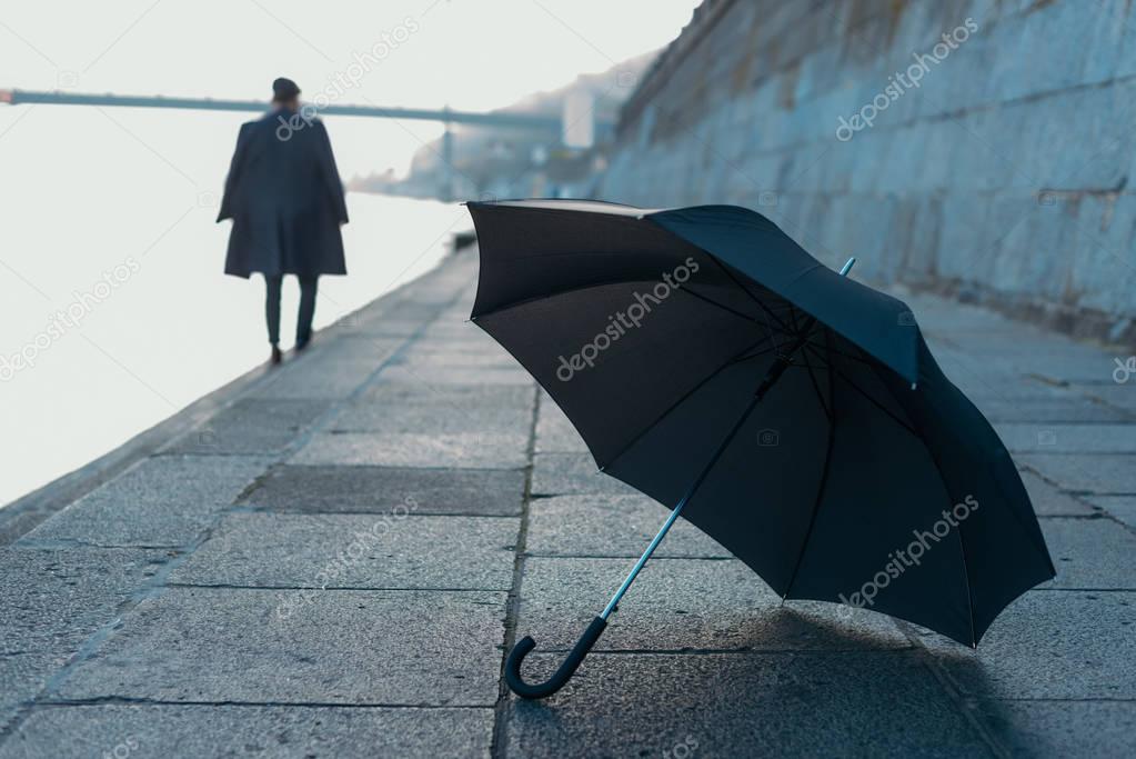 umbrella lying on river shore while man walking blurred on background